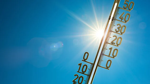 Thermometer zeigt Temperaturen über 30 Grad Celsius vor blauem Himmel mit Sonne an