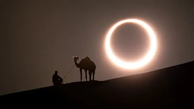 Ringförmige Sonnenfinsternis über der Wüste - Mann auf Düne mit Kamel