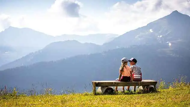 Zwei Kinder sitzen auf einer Bank und genießen die Aussicht auf das Alpbachtal