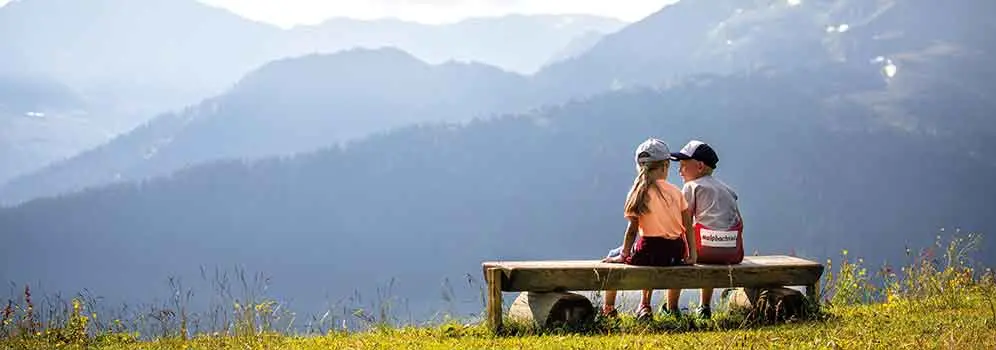 Zwei Kinder sitzen auf einer Bank und genießen die Aussicht auf das Alpbachtal