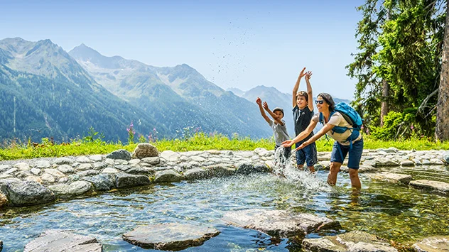 Eine Familie sucht erfrischt sich bei einer Wanderung im Wasser. 