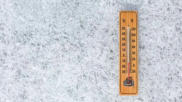 Thermometer liegt auf gefrorenem Boden und zeigt niedrige Temperaturen