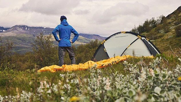 Wanderer in GORE-TEX Bekleidung beim Zelten in herbstlicher Berglandschaft.