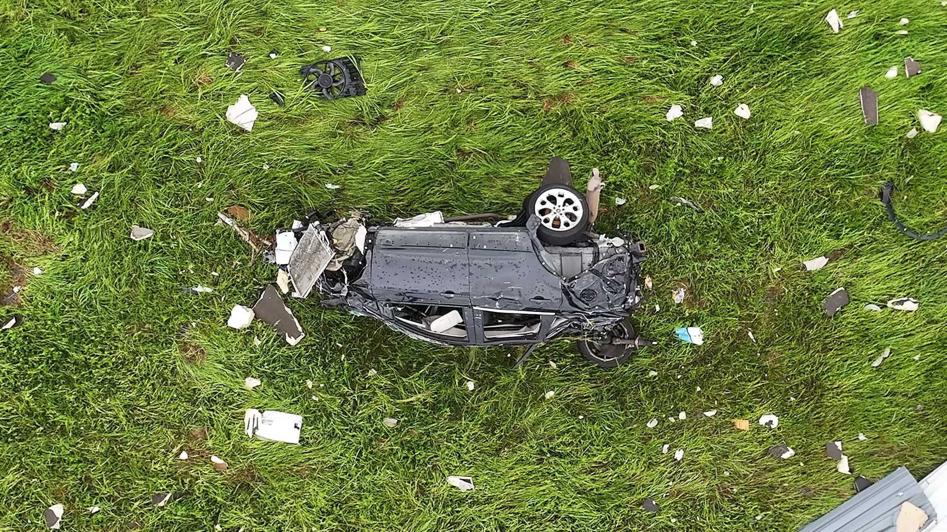 A car, completely totaled, lies in a field after likely being thrown by the violent winds of a tornado.