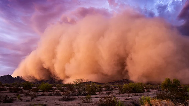 Bei Dämmerung fegt ein Sandsturm durch die Wüste. Die Staubwolke erreicht große Höhen.
