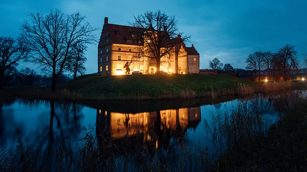 Bild: TMV/Petermann Das beleuchtete Schloss Ulrichshusen spiegelt sich im See.