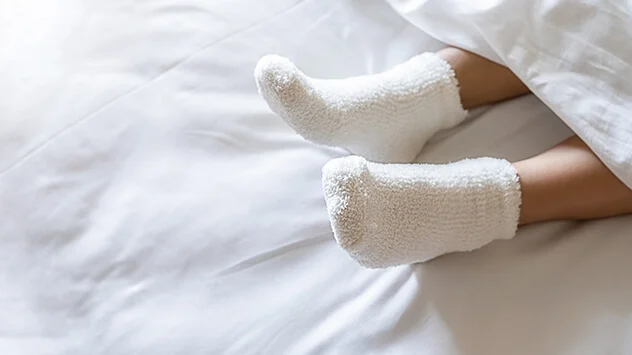 Füße mit warmen Socken gucken unter der Bettdecke hervor