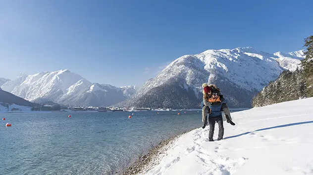 Mann trägt Frau auf dem Rücken am Ufer des Sees entlang.