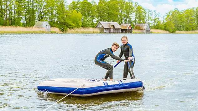 Kinder lassen sich von einem Hausboot auf ihrem Floss ziehen