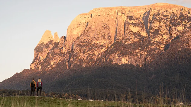 Herbstliche Highlights in den Dolomiten - Bild: Seiser Alm Marketing / Roschan Fill Wanderer blicken auf Bergkette, die von der tiefstehenden Sonne beleuchtet wird