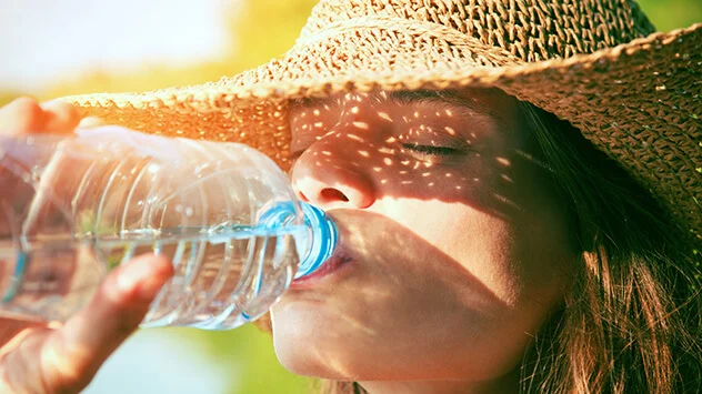 Frau mit Sonnenhut trinkt Wasser