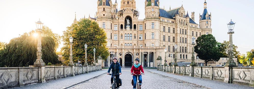 Schlosserlebnistour im Schweriner Umland - © TMV/Gross Ein radelndes Paar, im Hintergrund das Schweriner Schloss