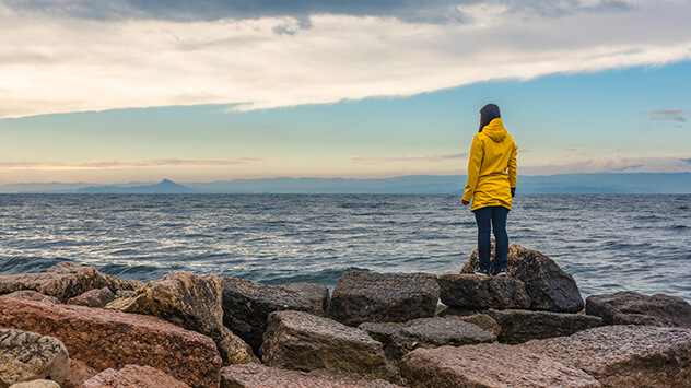 Frau im Regenmantel steht am Meer und stärkt ihr Immunsystem