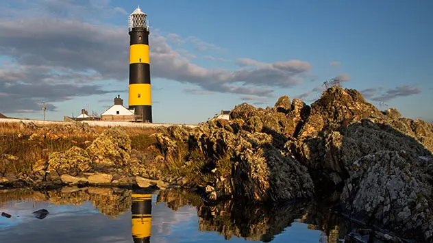 Schwarz-gelb gestreifter Leuchtturm von St John’s Point an der felsigen Küste von County Down.