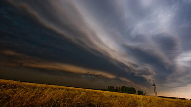 Bogenförmige dunkle Shelf-Cloud über Weizenfeld von untergehender Sonne angestrahlt