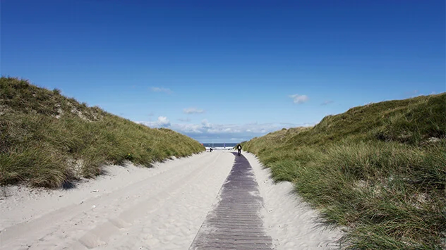 Strahlend blauer Himmel über dem Strandaufgang zwischen den Dünen