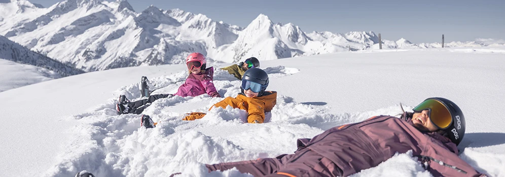 Kinder liegen auf dem Rücken im Schnee und genießen die Sonne