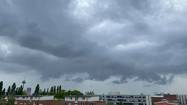 Ausgedehnte Schauer- und Gewitterwolken ziehen mit Wolkenfetzen über ein Kölner Wohngebiet