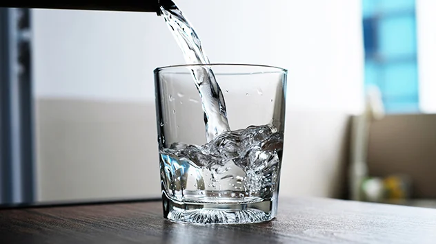 Ein Glas wird mit Wasser aus dem Wasserhahn aufgefüllt. 