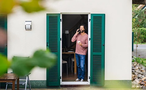 Workation auf der Ostseeinsel Poel - Bild: TMV/Gross Ein Mann steht an der Terrassentür seines Ferienhauses auf Poel und telefoniert.