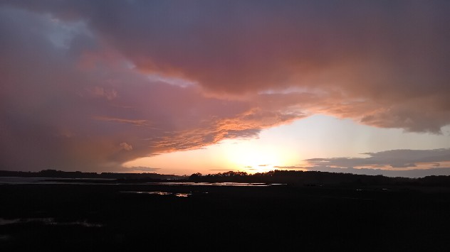 Sunset behind river, slightly obscured by rain clouds overhead