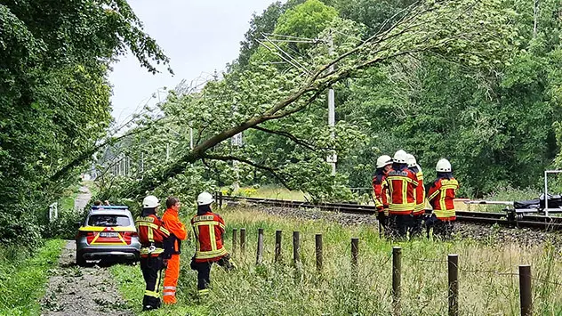 Einsatzkräfte der Feuerwehr stehen neben einem umgestürzten Baum über der gesperrten Bahnstrecke zwischen Oldenburg und Leer.