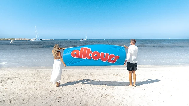 Zwei Personen mit alltours-Banner am Strand auf Mallorca.