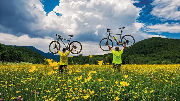 Zwei Radfahrer stehen in einer Blumenwiese mit ihren Rädern