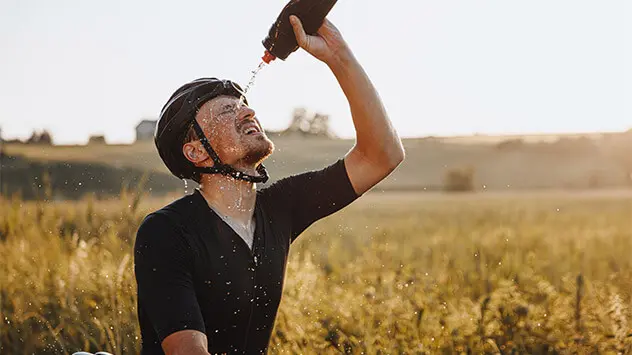 Ein Fahrradfahrer spritzt sich zur Erfrischung Wasser aus einer Flasche ins Gesicht. 