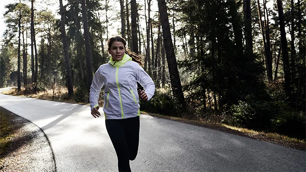 Läuferin in GORE-TEX Bekleidung auf einer Straße im Wald. 