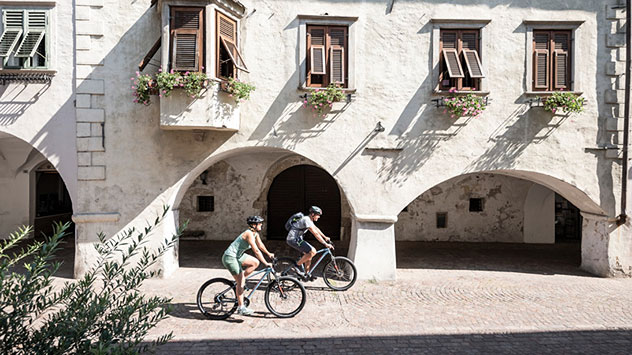 Zwei Radfahrer fahren durch einen historischen Ortskern von Neumarkt. 