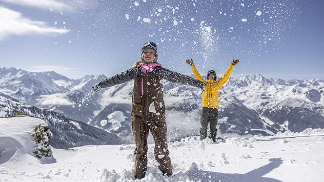 Zwei Skifahrer werfen Schnee in die Höhe. 