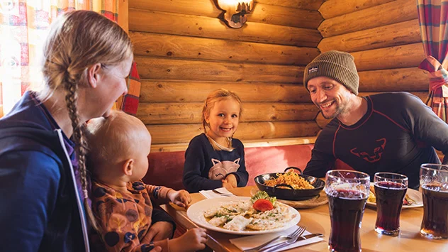 Eine Familie mit zwei Kindern genießt eine Mahlzeit in einer urigen Skihütte.