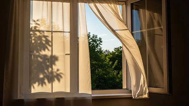 Vorhänge flattern an einem geöffnetem Fenster im Wind