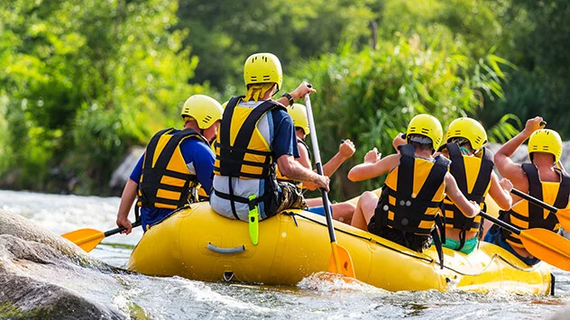 Gruppe sitzt in einem Rafting-Boot und paddelt auf einem Fluss
