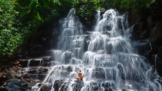Frau meditiert vor einem Wasserfall