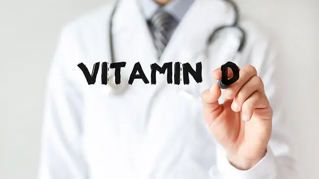 Person mit Arztkittel schreibt Vitamin D auf durchsichtige Scheibe.