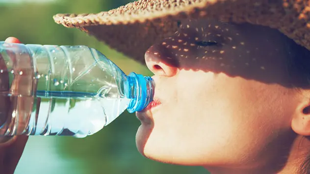 Frau mit Sonnenhut trinkt aus einer Wasserflasche