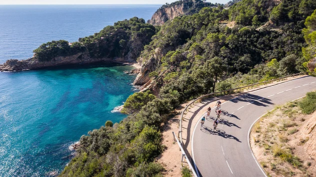 Rennradfahrer auf einer kurvigen Straße entlang der Küste mit Blick aufs Meer. 