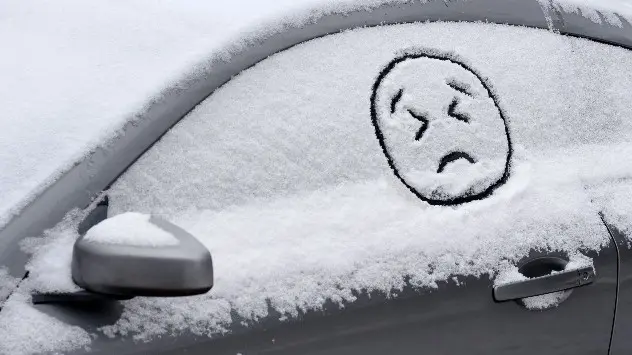 Sad face drawn in snow on car window