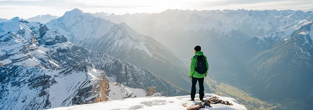 Wanderer blickt über verschneite Berggipfel