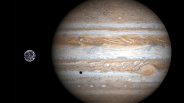 Jupiter im Vergleich zur Erde: Ein kleine Schatten auf den Wolken rührt von einer Sonnenfinsternis her. 