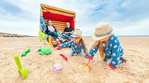 Eltern sitzen in Strandkorb, Kinder buddeln im Sand