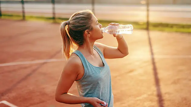 Sportliche Frau trinkt in der Sonne aus Wasserflasche