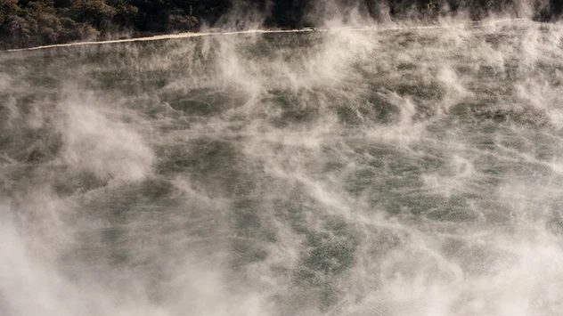 Dampf steigt über dem heißen Wasser eines Vulkansees auf.
