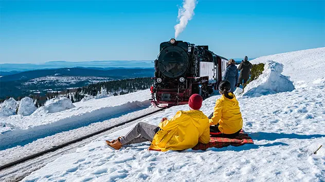 Wanderer im Schnee beobachten die Brockenbahn