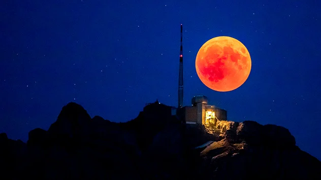 Beim Blut- und Kupfermond erscheint unser Erdtrabant orange bis rötlich. Über einem Berg zu sehen.