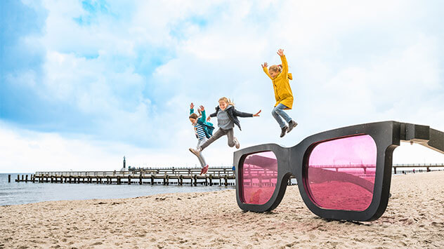 Kinder springen am Strand von Zingst über eine grosse Sonnenbrille