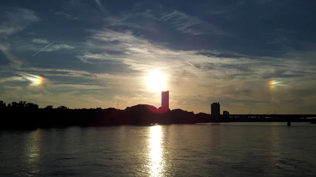 Zwei Nebensonnen neben einer tiefstehenden Sonne über eine Stadtsilhouette