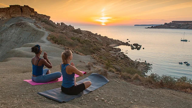 Zwei Frauen beim Yoga mit Blick auf das Meer und den Sonnenaufgang. 